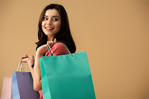 smiling and beautiful woman holding shopping bags isolated on beige