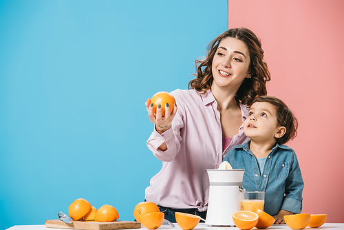 smiling mother showing whole orange to cute little son on bicolor background