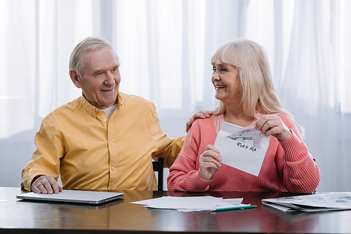 senior couple holding envelope with 'roth ira' lettering and money while sitting at table