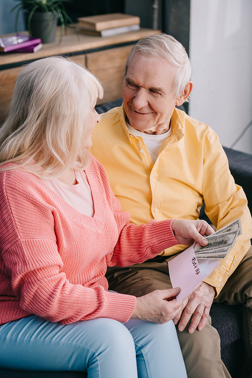 smiling senior couple holding envelope with 'roth ira' lettering and dollar banknotes