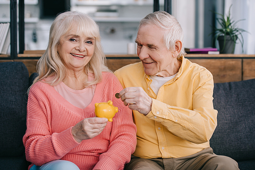 happy senior couple putting coin in yellow piggy bank