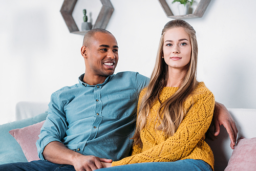 multicultural couple holding hands on sofa