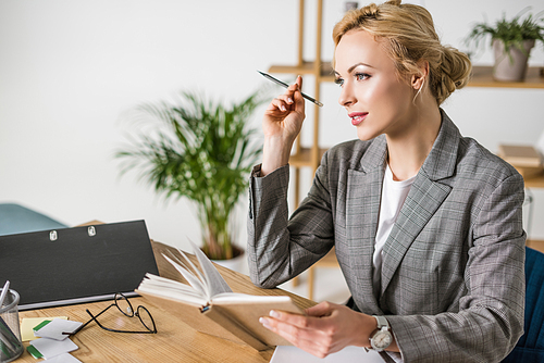 side view of pensive businesswoman with notebook at workplace