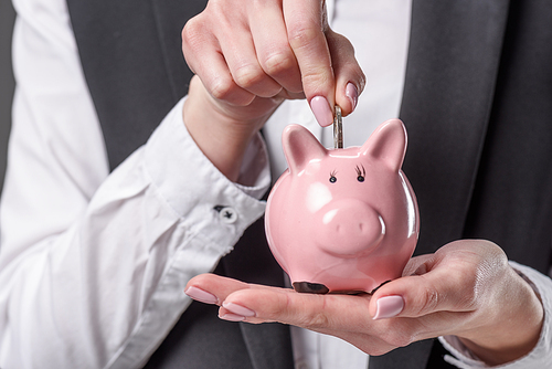 cropped shot of businesswoman putting coin into piggy bank isolated on grey