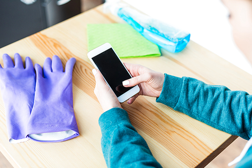 cropped shot of woman using smartphone with blank screen while cleaning house