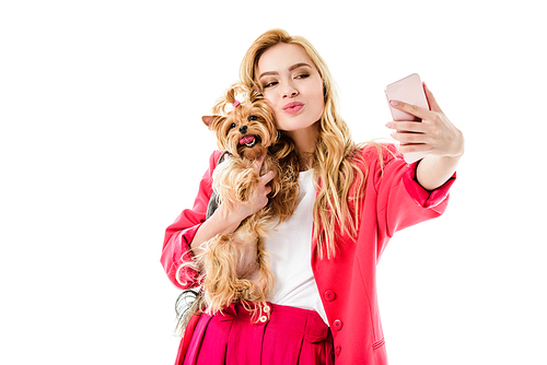 Young girl wearing pink suit holding cute Yorkshire terrier and taking selfie isolated on white