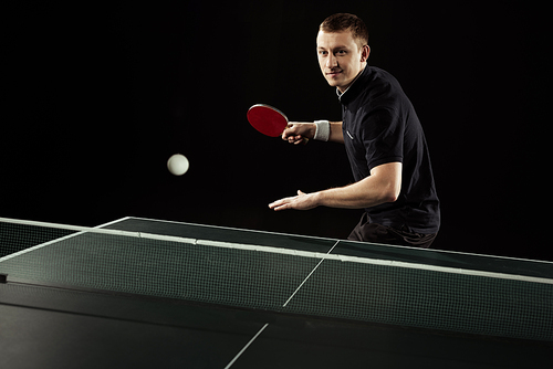 portrait of tennis player in uniform playing table tennis isolated on black