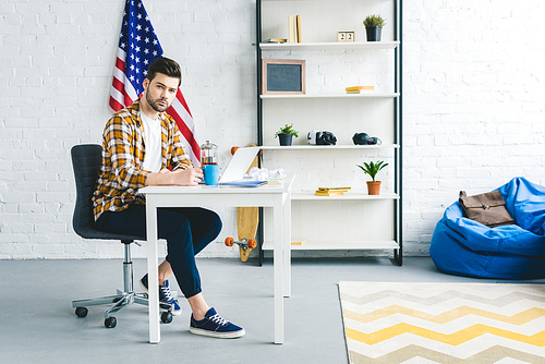 Young bearded man working by laptop in light office