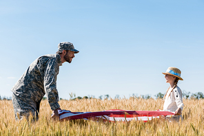 soldier in uniform and happy child holding american flag in field