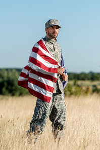 military man in camouflage uniform and cap holding american flag in golden field