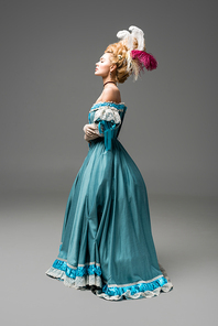side view of pompous victorian woman in wig standing in blue dress on grey