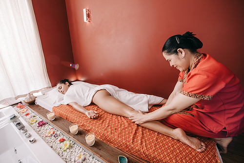 asian masseur doing foot massage to woman in spa salon