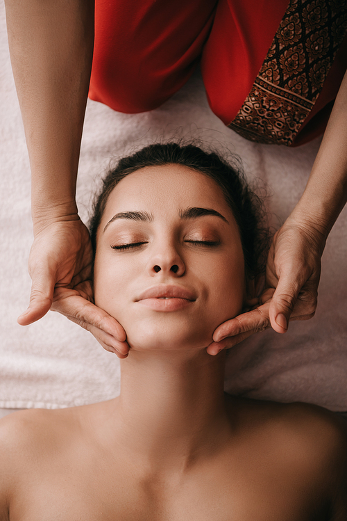 cropped view of masseur doing face massage to woman in spa salon