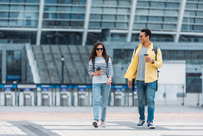 Woman walking near bi-racial friend with coffee paper cup and backpack