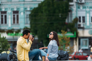 Bi-racial man sitting and taking photo of woman in sunglasses with backpack