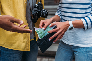 Cropped view of woman checking money in wallet near bi-racial friend