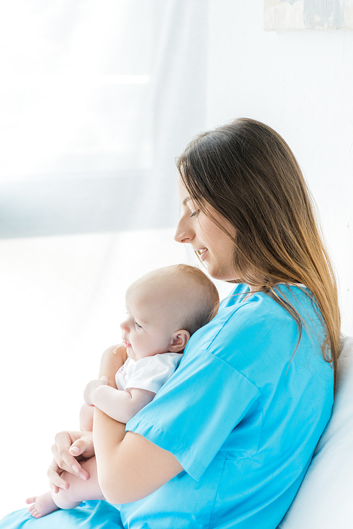 side view of attractive and young mother holding her child in hospital