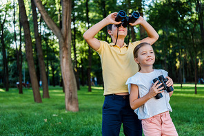 happy boy looking through binoculars near cute friend in park