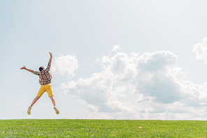 back view of boy jumping and gesturing against blue sky