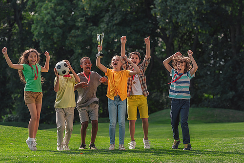 happy multicultural kids football and trophy in park