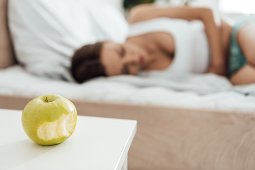 selective focus of suffering woman touching belly and green apple on foreground