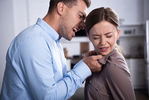 aggressive man in shirt screaming at scared wife at home