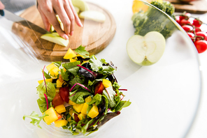 selective focus of glass bowl with salad near woman cutting apple