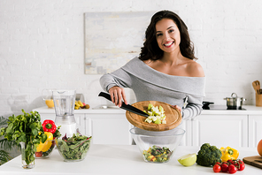 cheerful girl holding knife and cutting board near salad in bowl