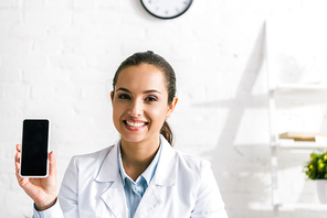 happy doctor in white coat  and holding smartphone with blank screen