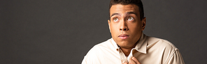 panoramic shot of handsome mixed race man in beige shirt feeling cold on black background