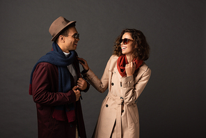 stylish interracial couple in autumn outfit laughing on black background