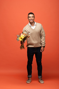 smiling mixed race man holding autumnal bouquet on orange