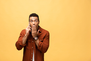 surprised mixed race man talking on smartphone isolated on yellow