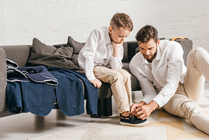 father sitting on carpet and tying shoelaces for son