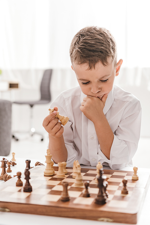 pensive boy in white shirt playing chess at home