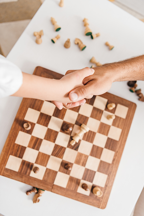 partial view of dad and son shaking hands over chessboard