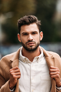 front view of handsome bearded man in stylish coat in autumn day on street