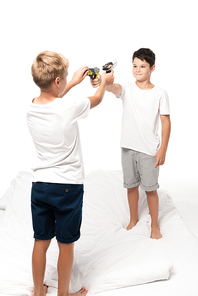 two brothers aiming at each other with toy guns while standing on bed isolated on white