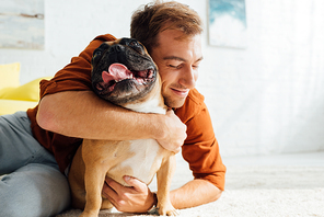 Smiling man hugging funny french bulldog on floor in living room