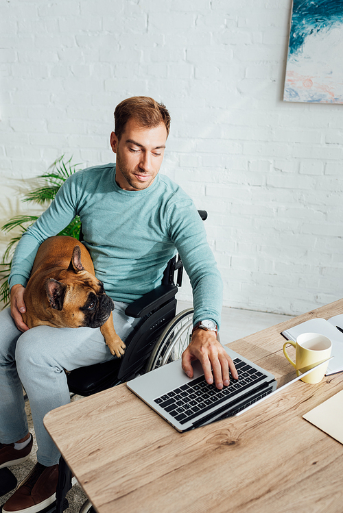 Disabled man holding french bulldog and working on laptop at home