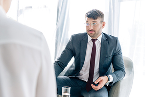 selective focus of handsome businessman in suit and glasses talking with journalist