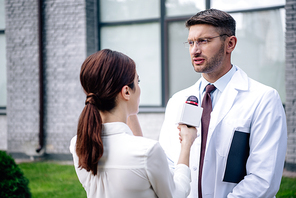journalist holding microphone and talking with handsome doctor in white coat