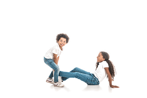 cheerful african american boy dragging sister by leg on white background