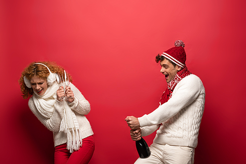 cheerful funny couple in winter outfit holding champagne for celebrating christmas, on red