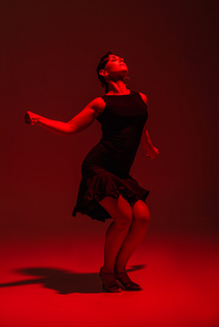 sensual dancer in black dress performing tango on dark background with red lighting