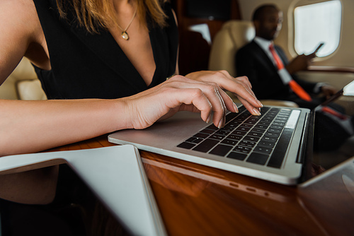 selective focus of businesswoman typing on laptop near african american businessman in plane
