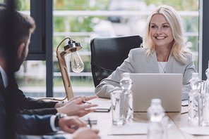 attractive businesswoman smiling during business meeting with young colleagues