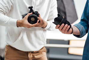 cropped view of photographer holding digital camera near art director with camera lens