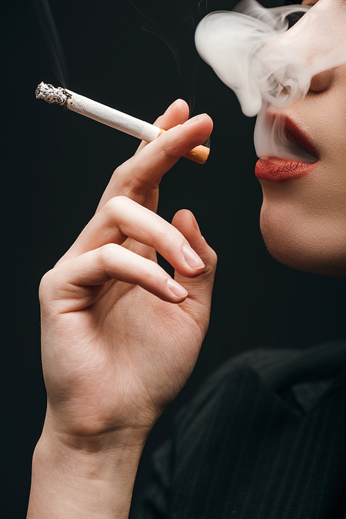 Cropped view of woman smoking cigarette isolated on black