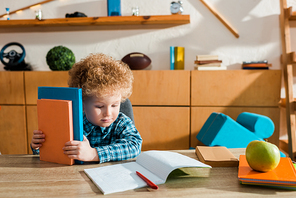 cute smart kid looking at notebook and holding books